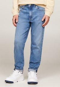 Jeans in denim azzurro chiaro con vestibilità dritta, dotati di tasche, chiusura con bottone e orli arrotolati, abbinati a sneakers bianche.
