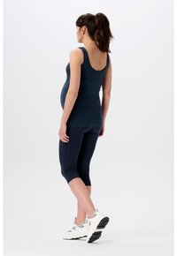 Zwangerschaps sportkleding met een nauwsluitend navy ribbel tanktop en bijpassende cropped leggings, gecombineerd met witte sportschoenen.