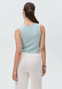 Svetlomodrá skrátená nátelník s textúrovanou tkaninou, s neupravenými okrajmi a okrúhlym výstrihom. Spárované s voľnými krémovými nohavicami.