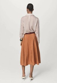 Gestreepte blouse met lange mouwen en kraag, gecombineerd met een vloeiende, roestrode rok met een textuurafwerking en een ceintuur om de taille.