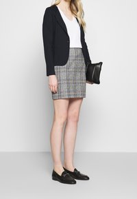 Blazer ajusté bleu marine sur un t-shirt blanc à col en V, associé à une jupe à carreaux dans des tons gris et bleu, et des mocassins noirs. Sac à main noir.