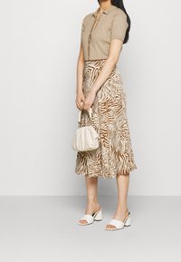 Maglione polo in beige, texture a costine; gonna midi a stampa zebra marrone e bianca; borsa crema; sandali con tacco a blocco bianchi.