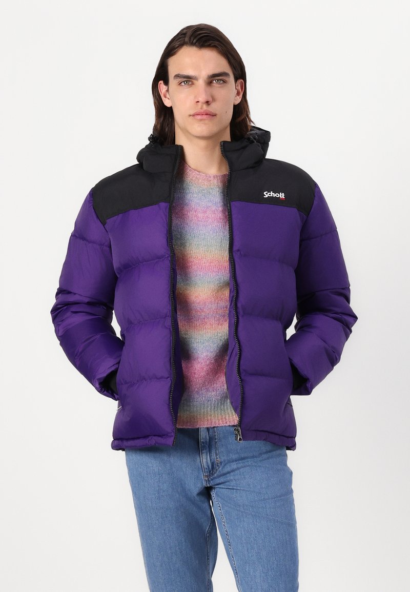 Giacca a vento viola con spalla e cappuccio neri. Presenta una cerniera frontale, tasche laterali e un logo sul petto. Indossata sopra un maglione multicolore.
