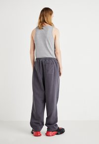 Grå tank top og løse, mørkegrå joggebukser med elastisk liv. Skoene er svarte med røde aksenter. Enkelt, avslappet design.