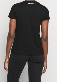 Černé bavlněné tričko s krátkým rukávem, přiléhavý střih a logo potisknuté na zadním výstřihu. V kombinaci s černými denimovými kalhotami.