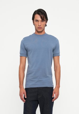 T-shirt in cotone blu, maniche corte con bordi arrotolati, collo a giro, tessuto leggero, design minimal e branding discreto sull'orlo.