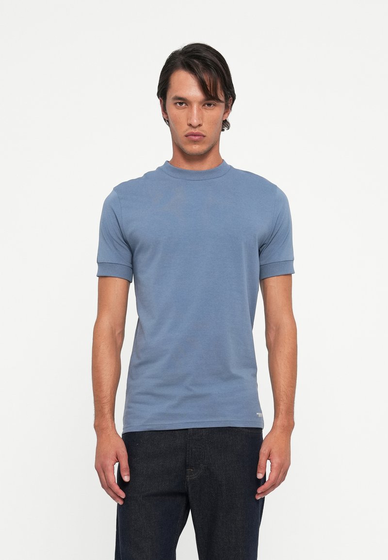 Blue cotton t-shirt, short sleeves with cuffed edges, crew neckline, lightweight fabric, minimal design, and subtle branding at the hem.