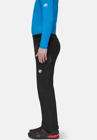 Sorte vandrebukser med lynlåslommer, tætsiddende ben og et logo på låret, parret med sorte og røde udendørssko.