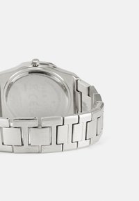 Ur i rustfrit stål med en poleret og børstet finish, der har et sammenkoblet armbånd og et rundt urkasse. Bagsiden er let synlig.
