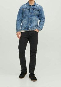 Ljusblå jeansjacka med klassisk design, som har två bröstfickor, slitna detaljer och svarta smala byxor med subtil textur.