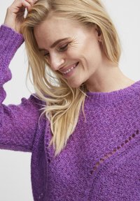 Pull en maille violet avec un motif texturé et des détails de points ouverts. Manches longues, coupe décontractée et encolure ronde. Tissu doux et chaud.