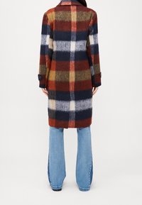 Cappotto in misto lana con un motivo tartan multicolore nei toni del blu navy, rosso e beige, dotato di colletto a scollo e polsini abbottonati.
