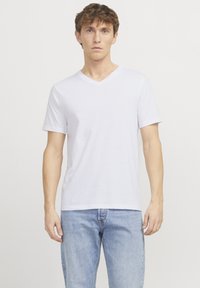 Weißes Baumwoll-T-Shirt mit V-Ausschnitt und kurzen Ärmeln, mit weicher Textur und entspannter Passform. Kombiniert mit hellblauen Denim-Jeans.