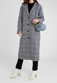 Cappotto a scacchi blu e bianco, con collare, chiusura a bottoni e tasche. Abbinato a pantaloni neri, stivaletti bianchi alla caviglia e una borsa rotonda blu.