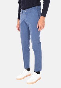 Chinos in cotone blu con una vestibilità slim, dotati di due tasche frontali e due chiusure con bottone. Indossati con sneakers bianche e calzini neri.