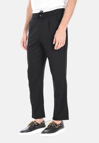 Pantaloni neri con una vestibilità rilassata, dotati di pieghe davanti, un elastico in vita con cordoncino e tasche. Abbinati a scarpe nere.
