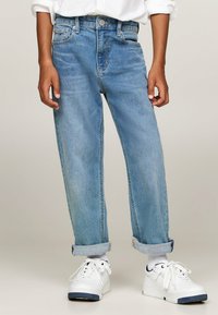 Jeans in denim azzurro con una vestibilità rilassata, caratterizzati da un'alta vita, orli risvoltati e passanti per cintura. Abbinati a sneakers bianche.