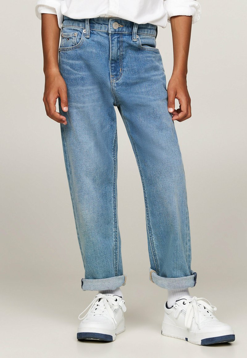 Jeans in denim azzurro con una vestibilità rilassata, caratterizzati da un'alta vita, orli risvoltati e passanti per cintura. Abbinati a sneakers bianche.