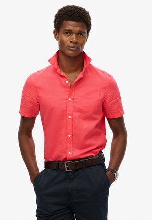 Koraalkleurig overhemd met korte mouwen en kraag, voorzien van een borstzak en een textuur, gedragen met een marineblauwe broek en een bruine riem.