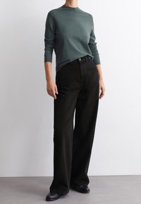 Mörkgrön, figursydd tröja med långa ärmar som matchas med högmidjade svarta vida jeans, accentuerad av en enkel knappstängning och platta skor.