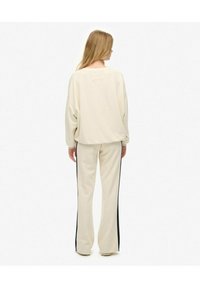 Crème-kleurige relaxed fit sweatshirt met verlaagde schouderlijnen en bijpassende broek met zwarte zijstrepen. Minimalistisch ontwerp en zachte textuur.