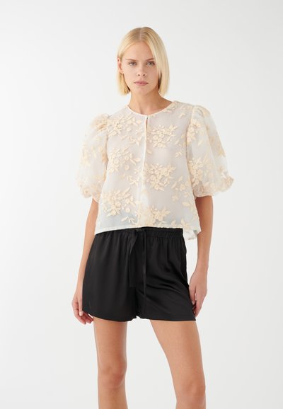 Haut transparent blanc avec broderie florale en beige clair, manches bouffantes et encolure ronde, associé à un short noir à taille élastique.