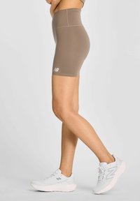 Brązowe szorty z wysokim stanem, wykonane z elastycznego materiału, o gładkiej fakturze, z białym logo New Balance na dolnej części nogawki.