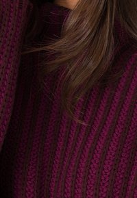 Pull en tricot avec des rayures marron foncé et violet profond, présentant un design texturé avec des motifs côtelés.