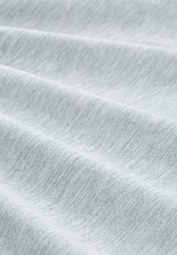 Jasnoniebieska, tkana tkanina o teksturowej powierzchni, z subtelnymi wariacjami w kolorze i wzorze, ułożona w miękkie fałdy.