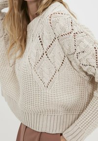 Béžový pletený svetr se vzory copánk ů a diamantů, žebrovanými manžetami a lemem, s texturovaným povrchem a volným střihem.
