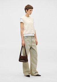 Πλεκτό κρεμ γιλέκο με κουμπιά πάνω από λευκό μπλουζάκι, συνδυασμένο με ανοιχτό πράσινα φαρδιά τζιν, καφέ τσάντα και μαύρα μυτερά παπούτσια.