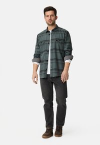 Grünes kariertes Hemd mit Knopfverschluss, weißes Unterhemd, schwarze Jeans und braune Sneaker, die einen lässigen, strukturierten Look zeigen.
