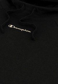 Sudadera negra de tela suave con capucha ajustable y un логотип dorado de "Champion" en el pecho. Textura suave, diseño minimalista.