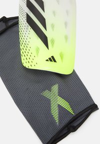 Geel en zwarte beschermende scheenbeschermer met een gestructureerd gradient ontwerp. Grijze mesh-sleeve met een groen gestreept logo en ademend materiaal.