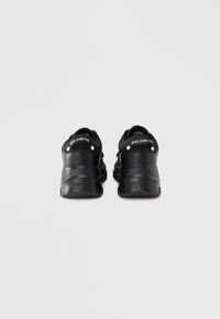 Černé tenisky z hladké kůže a gumového materiálu, s vyvýšeným podpatkem, logem na zadní straně a zaobleným tvarem.