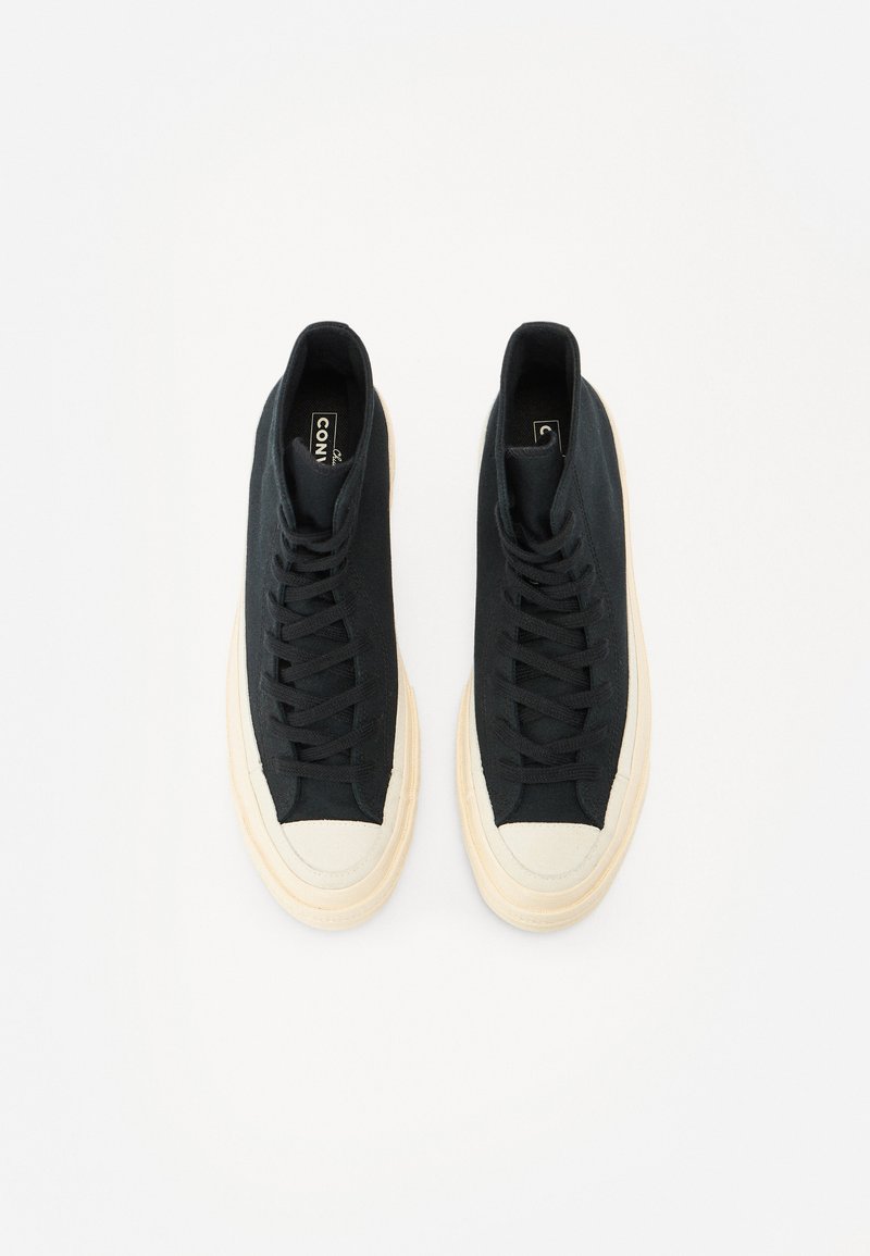 Zapatillas altas negras con un upper de tela texturizada, puntera de goma crema y suela translúcida. Los cordones pasan por ojales reforzados.