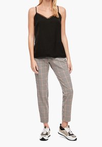 Svart linne med spetsdetaljer, i kombination med rutiga byxor i beige och svart, kompletterat med sneakers med vita, svarta och bruna accenter.