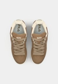 Baskets en suède marron avec des accents crème, dotées de lacets plats, d'un col rembourré et d'un détail logo sur la languette. Surfaces texturées visibles.