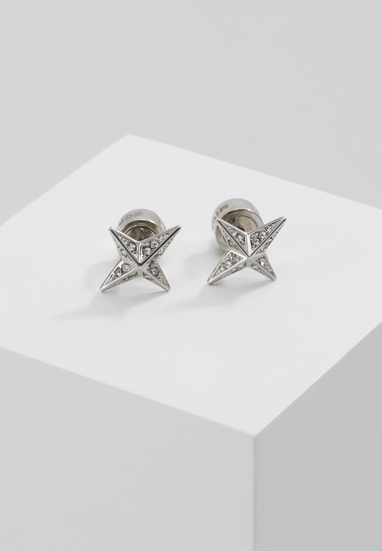Paire de boucles d'oreilles argentées en forme d’étoile avec de petits cristaux incrustés, présentées sur une surface blanche.