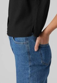 Czarny bawełniany top z bocznymi rozcięciami, zestawiony z niebieskimi jeansami denimowymi o klasycznym fasonie z pięcioma kieszeniami i widocznymi przeszyciami.