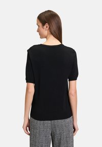 Maglione nero a maniche corte con scollo rotondo, caratterizzato da una morbida texture a maglia e una silhouette aderente. Accentuato da dettagli sulle spalle discreti.