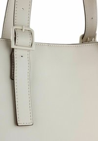 Borsa di colore chiaro con una texture di pelle liscia, caratterizzata da una tracolla rettangolare con fibbia e dettagli di cucitura a contrasto.