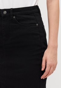 Gonna di jeans nera con vita alta, tasche laterali, bottone frontale e accessori in argento. Presenta un tessuto liscio e testurizzato.