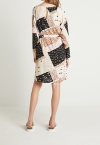 Vestido de manga larga, con abertura en la espalda y patrones mezclados en negro, crema y durazno. Cuenta con una cintura ceñida y acentos florales.