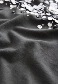 Black fabric with a smooth texture features scattered metallic sequins in silver and black, creating a shimmering effect across the surface.