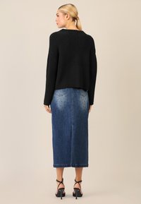 Schwarzer gerippter Strickpullover, knielanger Jeansrock mit heller Waschung und Nietenakzenten, kombiniert mit schwarzen Riemchenheels.