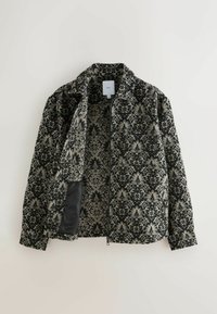 Schwarze und graue gemusterte Jacke mit floralem Damaskusdesign, der Reißverschluss vorne teilweise geöffnet, sodass das passende Innenfutter und die schwarze Tasche sichtbar werden.