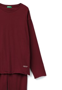 Camisa de manga larga burdeos en algodón suave con cuello redondo. Presenta un dobladillo sin acabar y un pequeño logo cerca del dobladillo inferior en el costado.