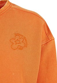 Sweatshirt orange avec motif de fleur brodée et texte "urban classics 05" sur la poitrine, montrant la couture de l'épaule et le détail du col.