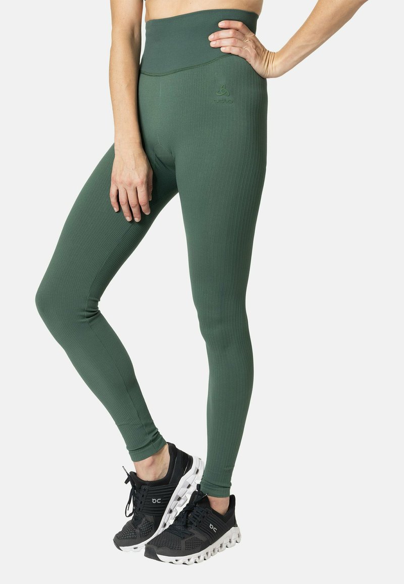 Grüne gerippte Leggings mit hohem Bund, versehen mit einem kleinen Logodetail. Getragen mit schwarzen Sneakers mit weißen Sohlen und Schnürsenkeln.
